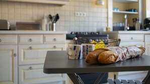 Ett kök med vita skåp, en brödrost, en kaffebryggare och en korg med bröd och muggar.