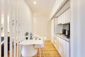 A modern kitchen with white cabinetry, a dining table with chairs, and a small island with a plant and water bottles. - January's 31 Studio by DA'HOME (Porto)
