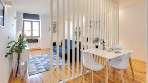 Ein modernes Zimmer mit einer weißen Trennwand, einem Esstisch mit Stühlen, einer Couch und einem blauen Teppich.