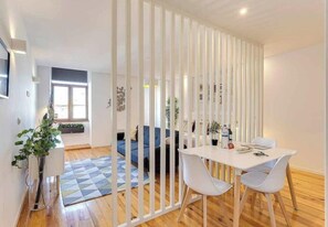 A modern room with a white partition, a dining table with chairs, a sofa, and a blue rug. - January's 31 Studio by DA'HOME (Porto)