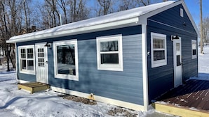 A small, single-story house with a dark blue exterior, white trim, and a covered porch area. - Cozy & Private Lakeside Cabin on Lake Irene – Swim, Fish, Relax (Parkers Prairie Douglas County)