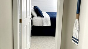 A narrow hallway leading to a bedroom with a bed, a door, and a broom leaning against the wall. - Cozy & Private Lakeside Cabin on Lake Irene – Swim, Fish, Relax (Parkers Prairie Douglas County)
