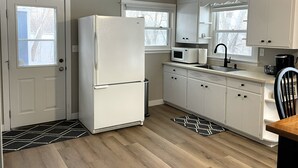 Una cucina compatta con mobili bianchi, un frigorifero, un forno a microonde e un lavello.