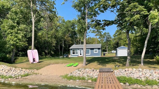 A wooden dock extending into a pond with a house and a shed in the background. - Cozy & Private Lakeside Cabin on Lake Irene – Swim, Fish, Relax (Parkers Prairie Douglas County)