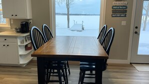 A dining area with a wooden table and chairs, a view of a snowy landscape through a door, and a wall with motivational signs. - Cozy & Private Lakeside Cabin on Lake Irene – Swim, Fish, Relax (Parkers Prairie Douglas County)