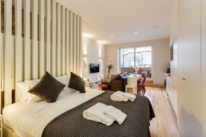 A modern bedroom with a large bed, a desk, and a view of the outdoors.