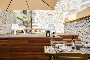 An outdoor dining area with wooden tables and chairs, stone walls, and a stone floor.