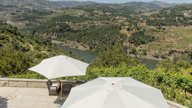 Una terrazza con posti a sedere all'aperto e ombrelloni, affacciata su un fiume e un paesaggio collinare.