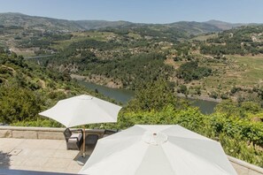 Una terrazza con posti a sedere all'aperto e ombrelloni, affacciata su un fiume e un paesaggio collinare.