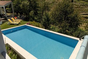 A rectangular swimming pool with a tiled edge, surrounded by a white pool deck. There are yellow lounge chairs aligned along the pool's edge.