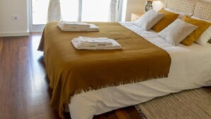 Un letto rifatto con cura, coperto da una tenda marrone e con cuscini bianchi, una lampada da comodino e un quadro incorniciato al muro.