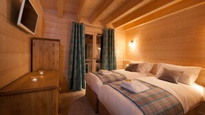 A wooden cabin bedroom with two beds, a wooden dresser, a TV mounted on the wall, and a door leading to another room. - Chalet Poudreuse (Morzine)