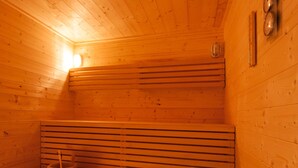 A wooden sauna with benches, a bench heater, and a wall-mounted thermometer. - Chalet Poudreuse (Morzine)