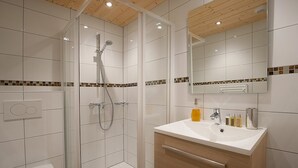 A modern bathroom with a glass-enclosed shower, a white sink with toiletries, and a wooden ceiling. - Chalet Poudreuse (Morzine)