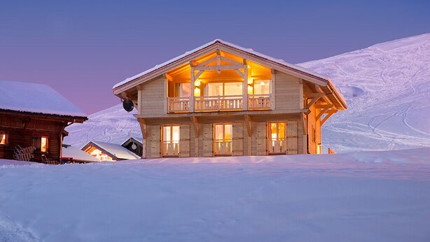 A two-story wooden chalet with a balcony, set against a snowy mountain backdrop. - Chalet Poudreuse (Morzine)