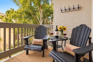 A balcony with two Adirondack chairs, a small table, a bottle of wine, and sunflowers.