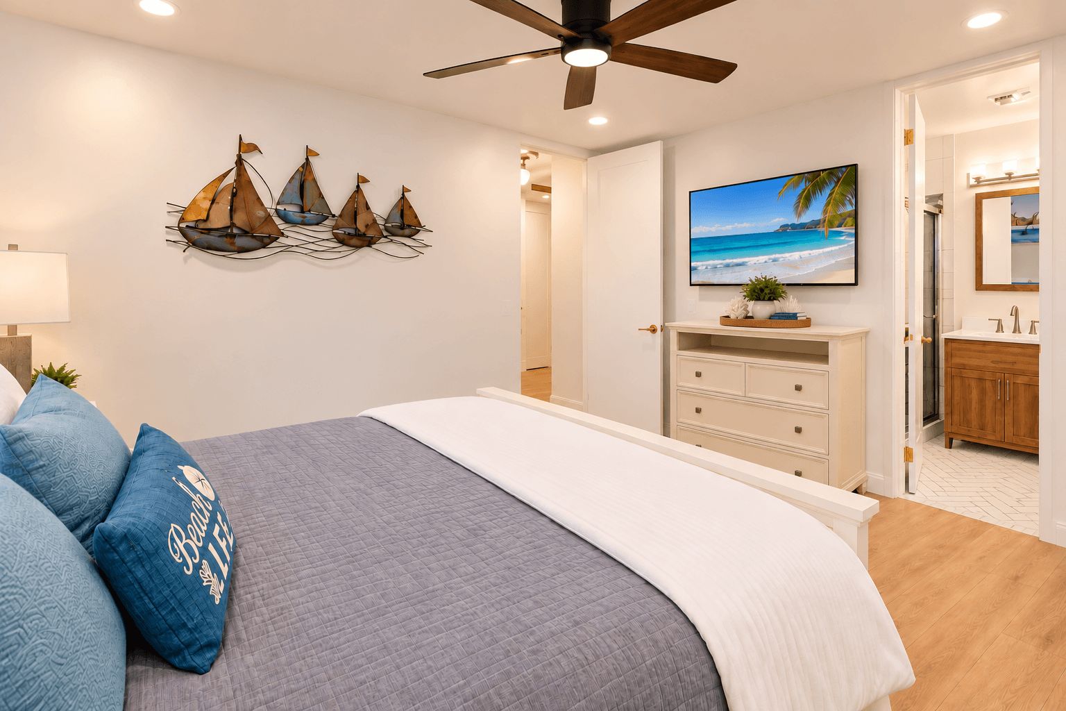 Une chambre à coucher comprenant un lit, un ventilateur de plafond, un téléviseur fixé au mur et une décoration murale représentant un voilier.