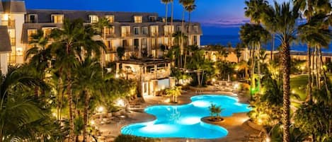 A resort with a large pool, palm trees, and a building with multiple windows.