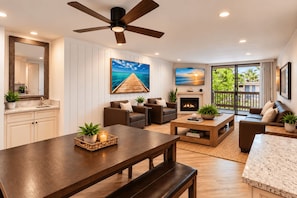 A spacious living room with a fireplace, comfortable seating, a dining area, and a large window offering a view of the outdoors. - Spacious 2BR Beach Condo | North Coast Village (Oceanside)