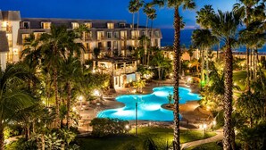 A resort with a pool area, palm trees, and a building with balconies. - 2BR Condo at North Coast Village | B116 (Oceanside)