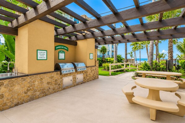 Un espace barbecue extérieur agrémenté de murs en pierre, d’une pergola et offrant une vue sur la plage.