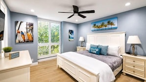 A bedroom with a bed, nightstands, a ceiling fan, and artwork on the walls.