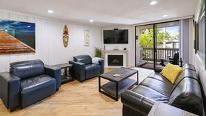 A modern living room with leather sofas, a fireplace, a large TV, and a view of the outdoors. - 2BR Condo at North Coast Village | B116 (Oceanside)