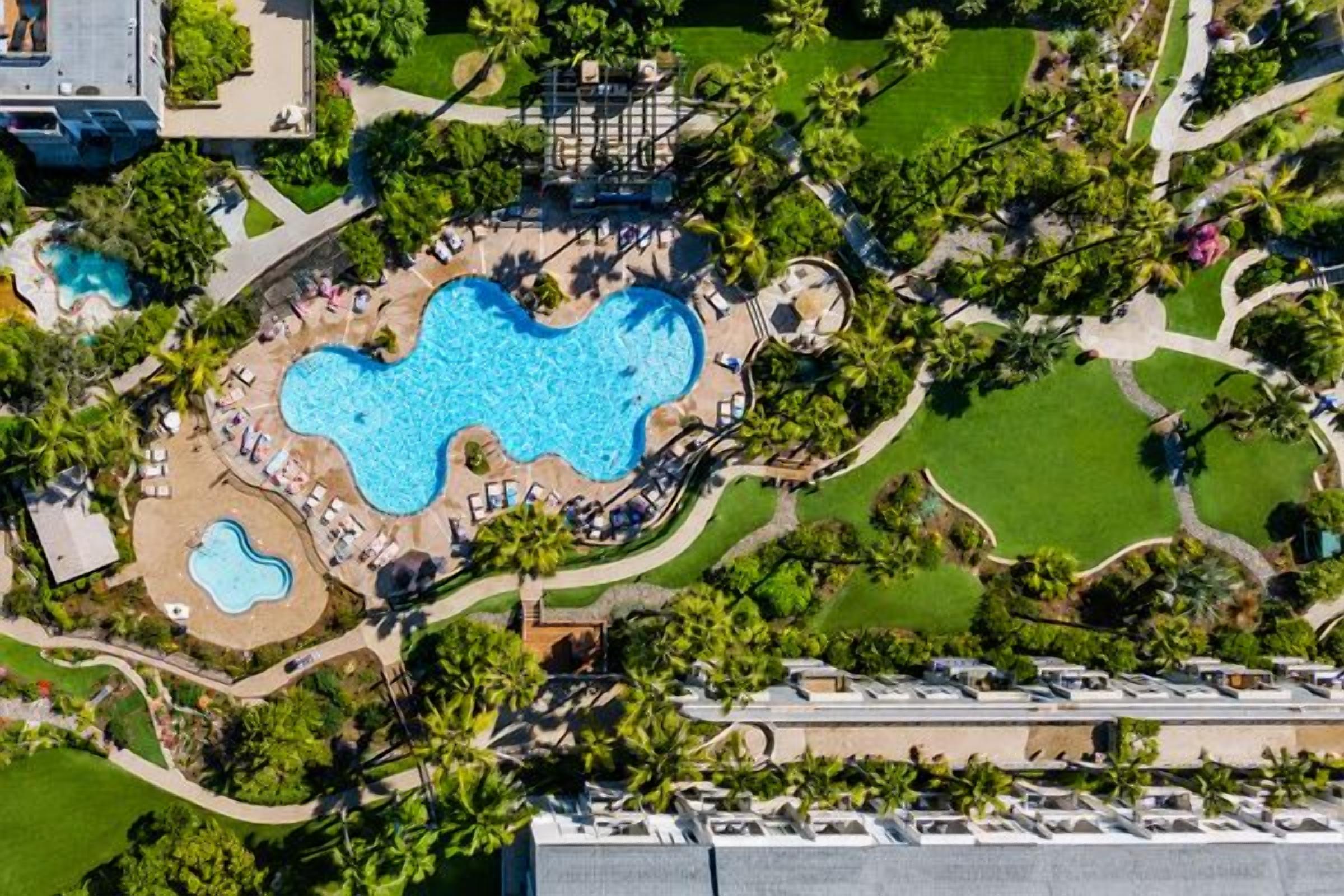 An aerial view of a hotel with a central swimming pool, surrounded by landscaped areas and pathways.