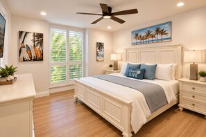 Une chambre à coucher avec un lit, des tables de chevet, un ventilateur de plafond et des œuvres d’art accrochées aux murs.