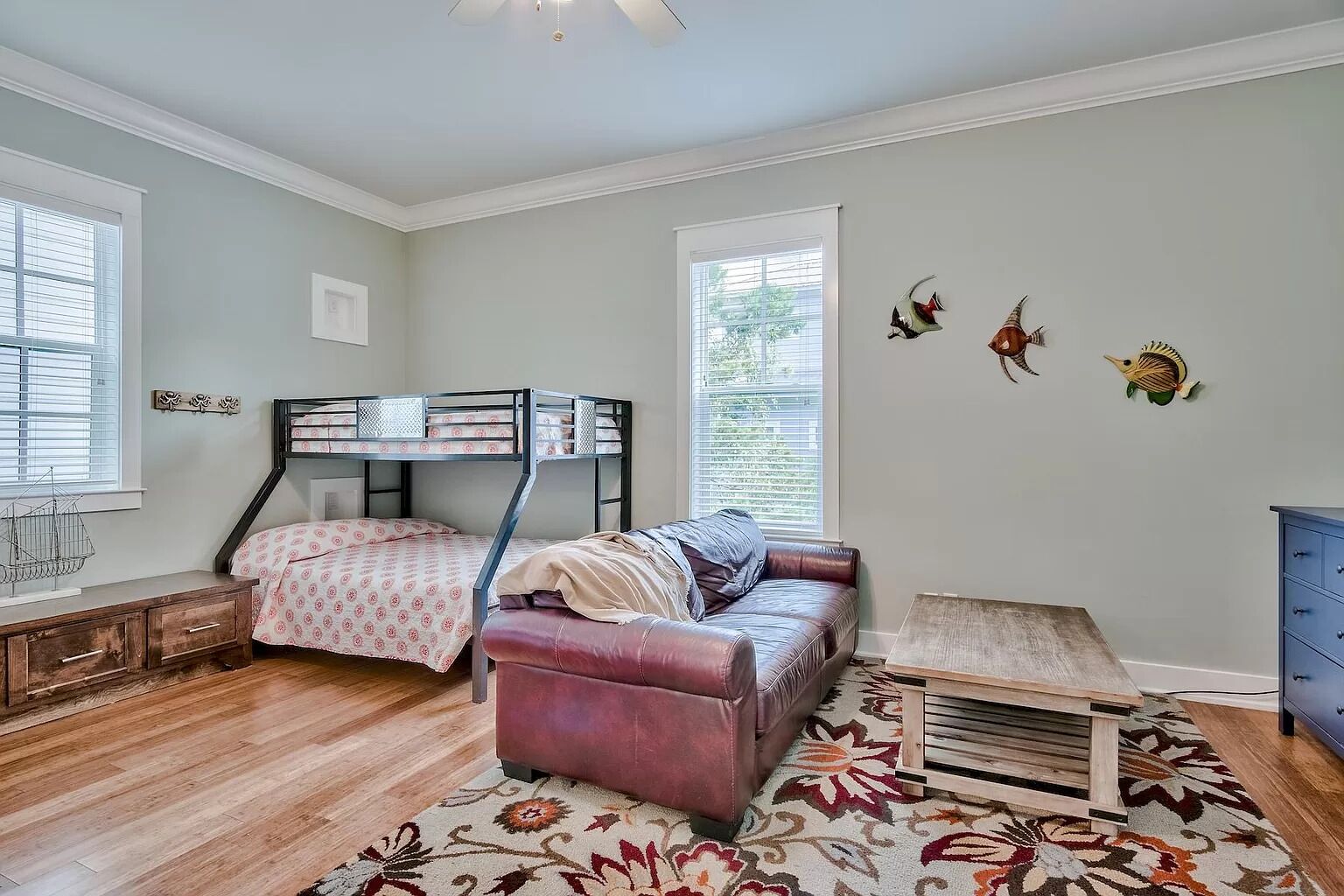 A bedroom with a bunk bed, a leather sofa, a wooden table, and decorative wall art.