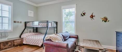 A bedroom with a bunk bed, a leather sofa, a wooden table, and decorative wall art.