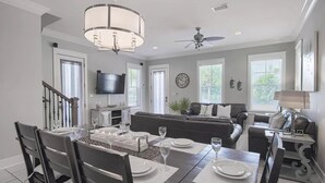 A dining area with a table set for six, a sofa, a TV, and a ceiling fan.