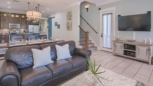 A modern living room with a leather sofa, a dining area, a kitchen, and a staircase.