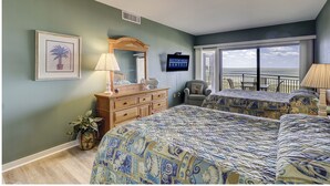 Une chambre avec un lit, une commode, un miroir, une télévision et une vue sur la plage.