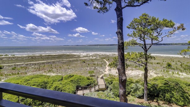 Une vue sur la côte, avec un ciel dégagé, une plage de sable et un sentier en bois menant à une construction.