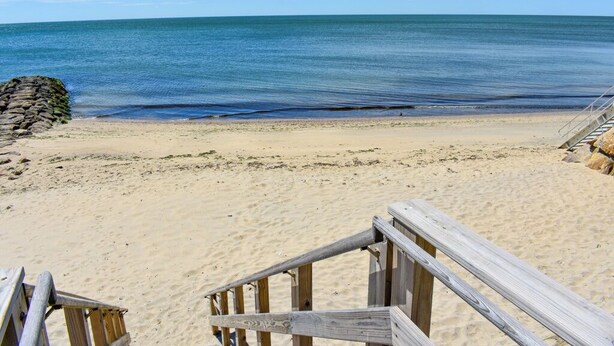 Una playa arenosa con una escalera de madera que baja al agua.