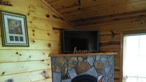 A wooden cabin interior with a stone fireplace, a television mounted above it, and a baby rocker in front of the fireplace. - Holidays are over!!! Come relax and unwind at Magnificent Views in Murphy!!! (Murphy)