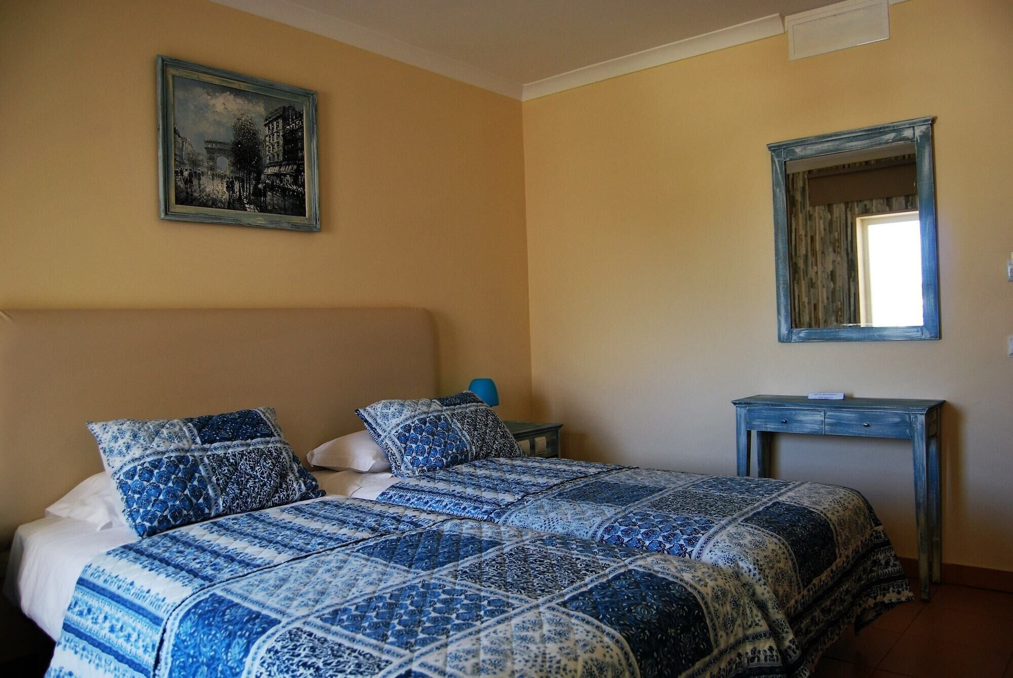 A bedroom with a bed, a nightstand, a dresser, a mirror, and a painting on the wall.