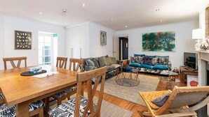A modern living room with a wooden dining table, a sofa, and a large abstract painting. - Lovely flat in Chelsea (London)
