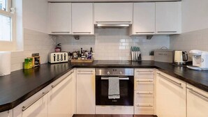 A modern kitchen with white cabinets, a Bosch dishwasher, and a coffee maker. - Lovely flat in Chelsea (London)