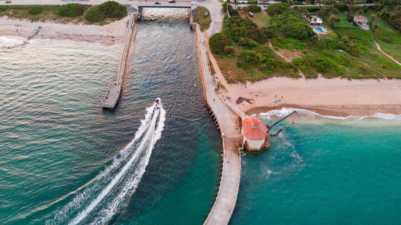Vista aèria d'una zona costanera amb un moll que s'endinsa a l'aigua, una platja i un pont.