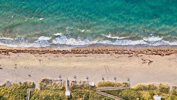 Vue aérienne d’une plage où l’on distingue clairement la ligne de rivage, un espace de stationnement et un chemin menant à la plage.