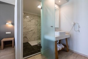 Un baño moderno con cabina de ducha de vidrio, un lavabo blanco y una pared de ducha de mármol.