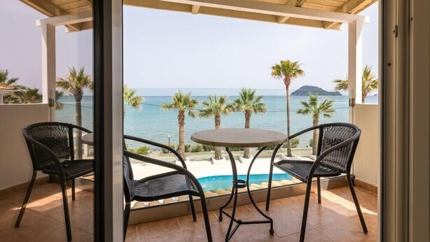 A balcony with a table and chairs, overlooking a pool and the sea. - Arkadianos Aparthotel (Zakynthos)