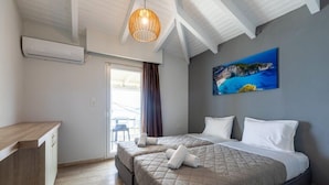A hotel room with two beds, a desk, and a painting of a coastal landscape. - Arkadianos Aparthotel (Zakynthos)