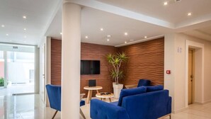A modern lobby with a blue sofa, a TV, and a plant. - Arkadianos Aparthotel (Zakynthos)