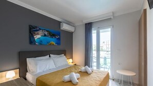 A hotel room with a bed, a painting, an air conditioning unit, a balcony with a table and chairs, and a small stool. - Arkadianos Aparthotel (Zakynthos)