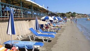 A beach with rows of sun loungers and umbrellas, a sandy shore, and a clear sky. - Arkadianos Aparthotel (Zakynthos)