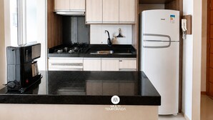 A modern kitchen with a black countertop, stainless steel appliances, and light wood cabinetry. - Nautilus Ap Vista Mar (Penha)
