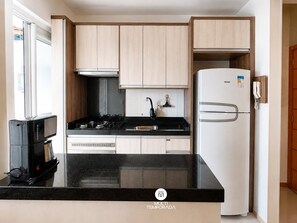A modern kitchen with a black countertop, stainless steel appliances, and light wood cabinetry. - Nautilus Ap Vista Mar (Penha)